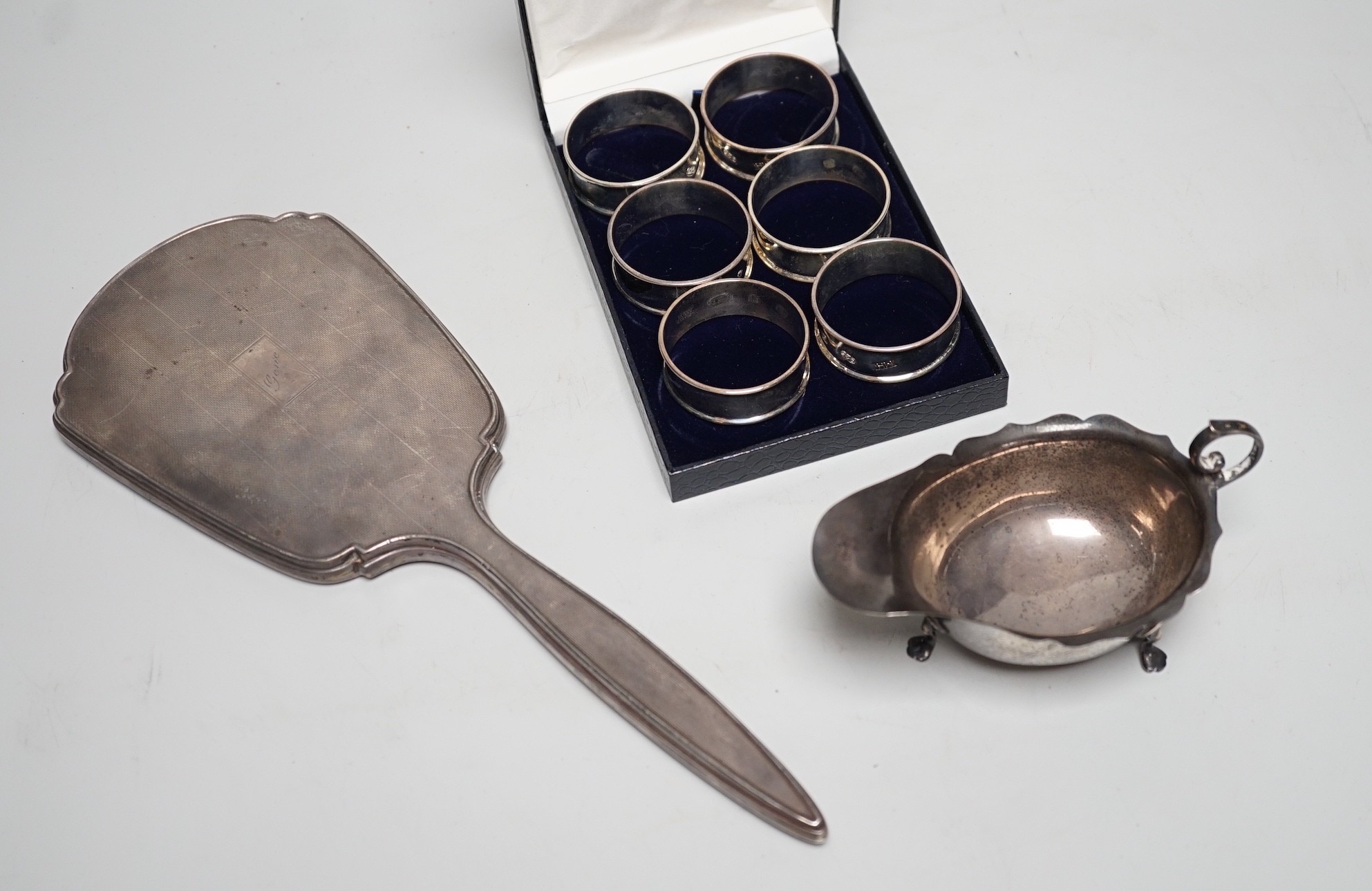 A set of six modern silver napkin rings, a George V silver sauceboat and a silver mounted hand mirror.